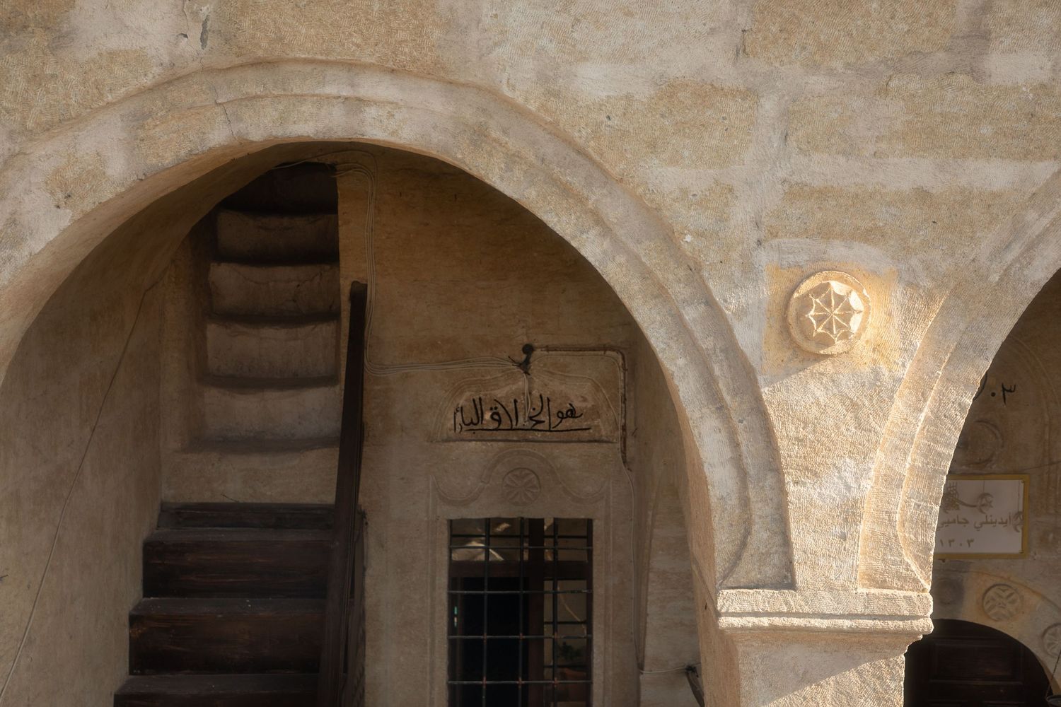 Historic stone archway with wooden staircase and decorative carved rosette in an ancient building.