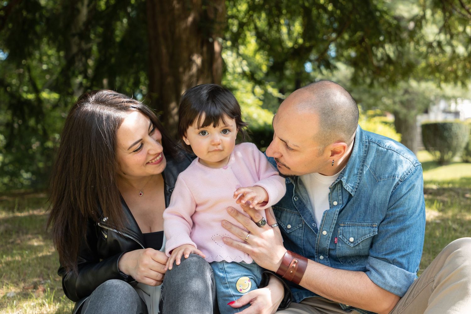 Happy family with toddler sitting together in lush green park outdoors.