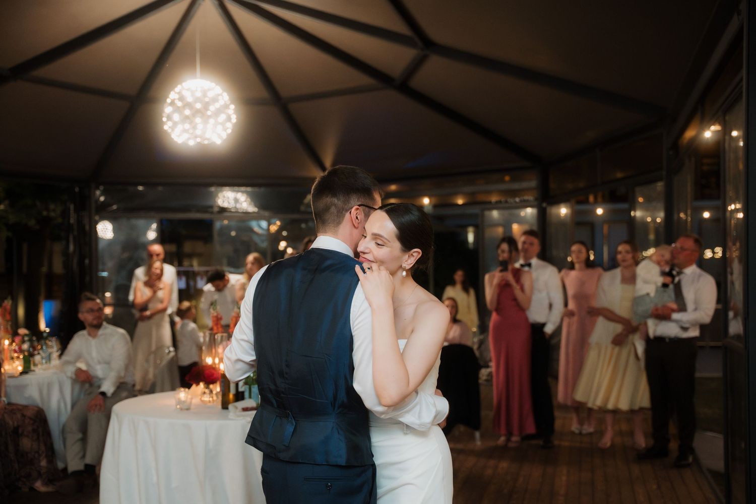 Bride and groom share a romantic first dance while guests watch at an evening reception.