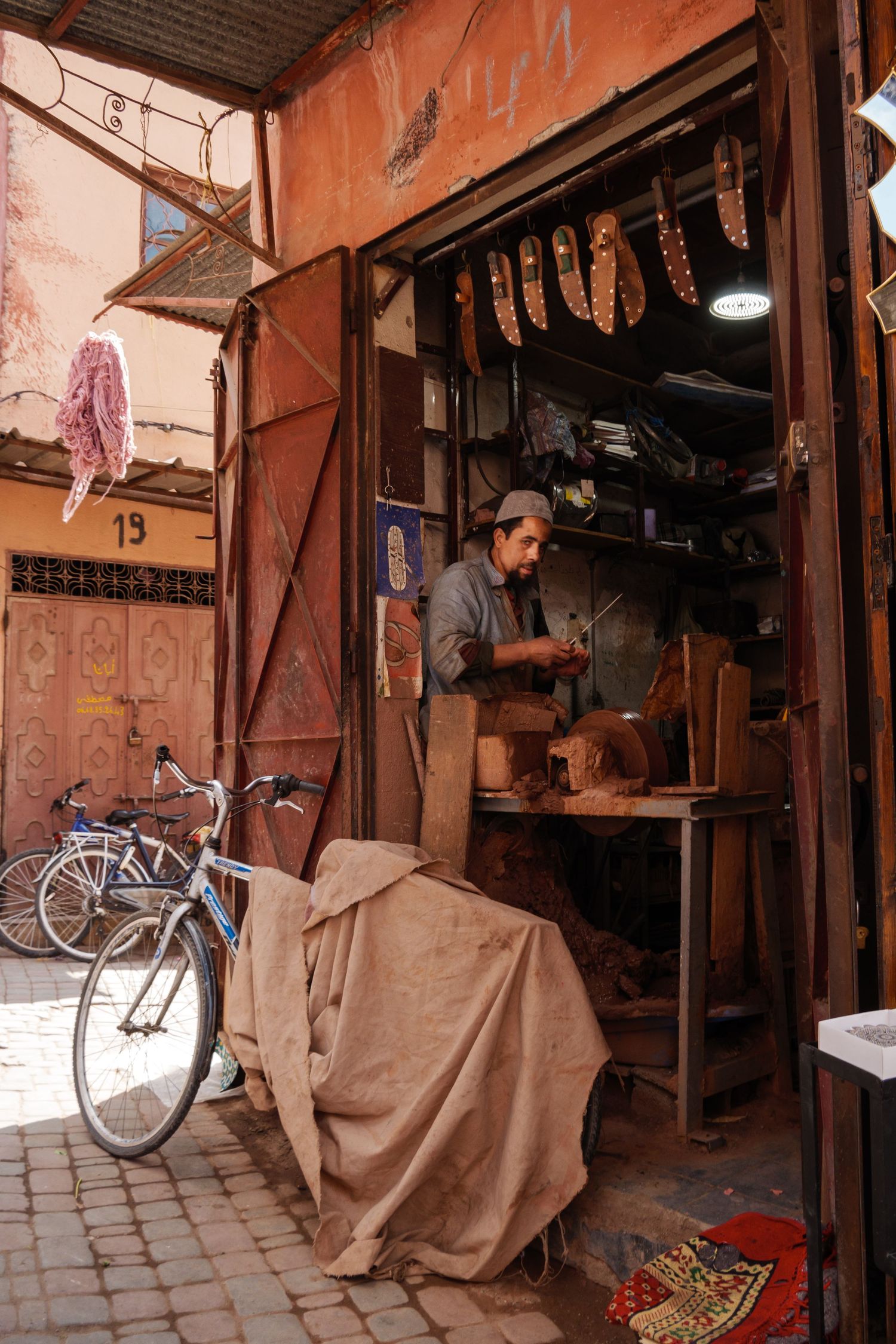 Moroccan craftsman working in a traditional workshop in the medina of Marrakech with bicycles outside.