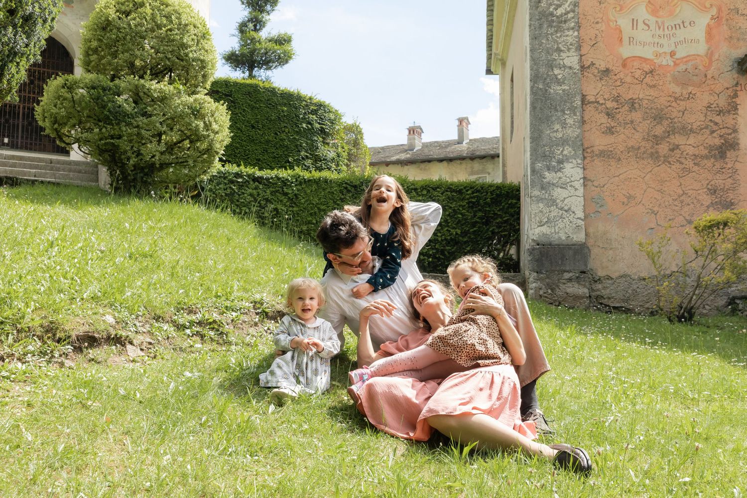 Happy family relaxing and laughing together on green grass in sunny garden.