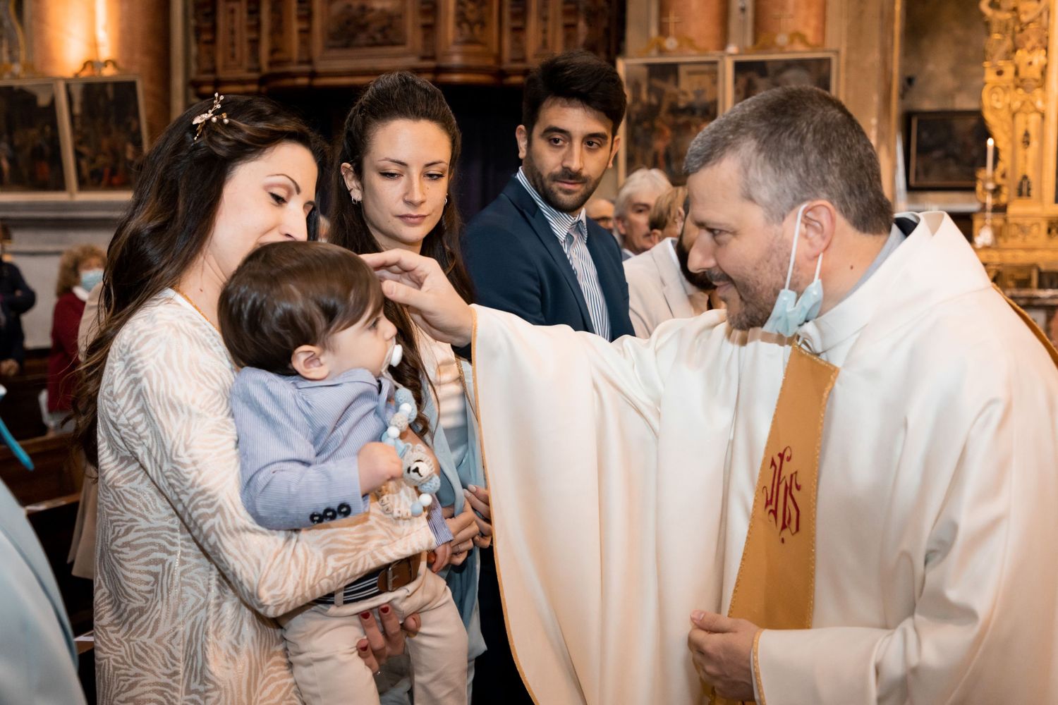 Priest blessing a baby held by the mother during a Catholic baptism ceremony in a church.