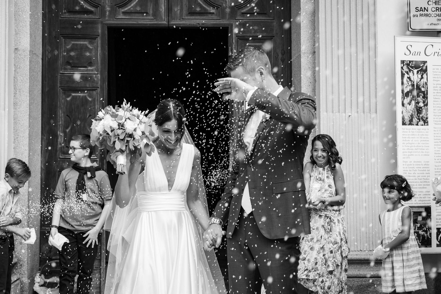 Newlyweds exit church as guests shower them with confetti in black and white photo.
