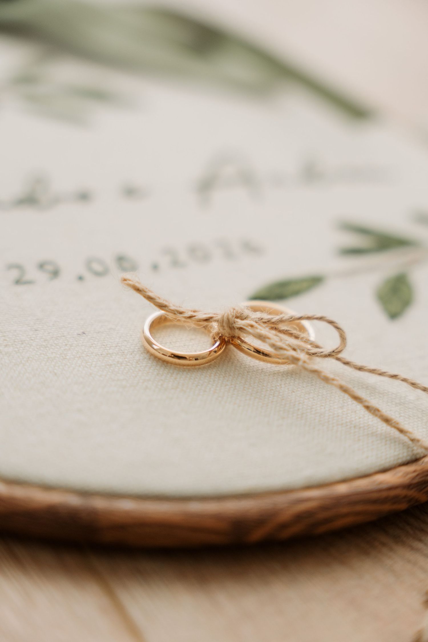 Two gold wedding rings tied with twine on an embroidered hoop with floral design and wedding date 29.08.2025.