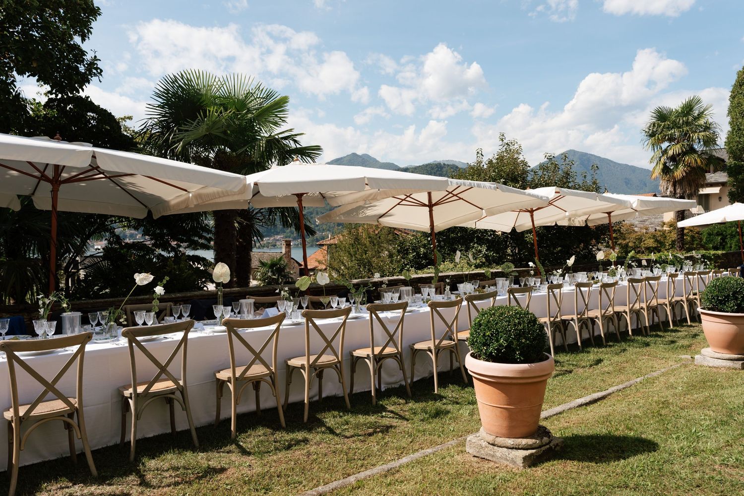 Elegant outdoor wedding reception with long tables, white umbrellas, cross-back chairs, and mountain views at a luxury villa.