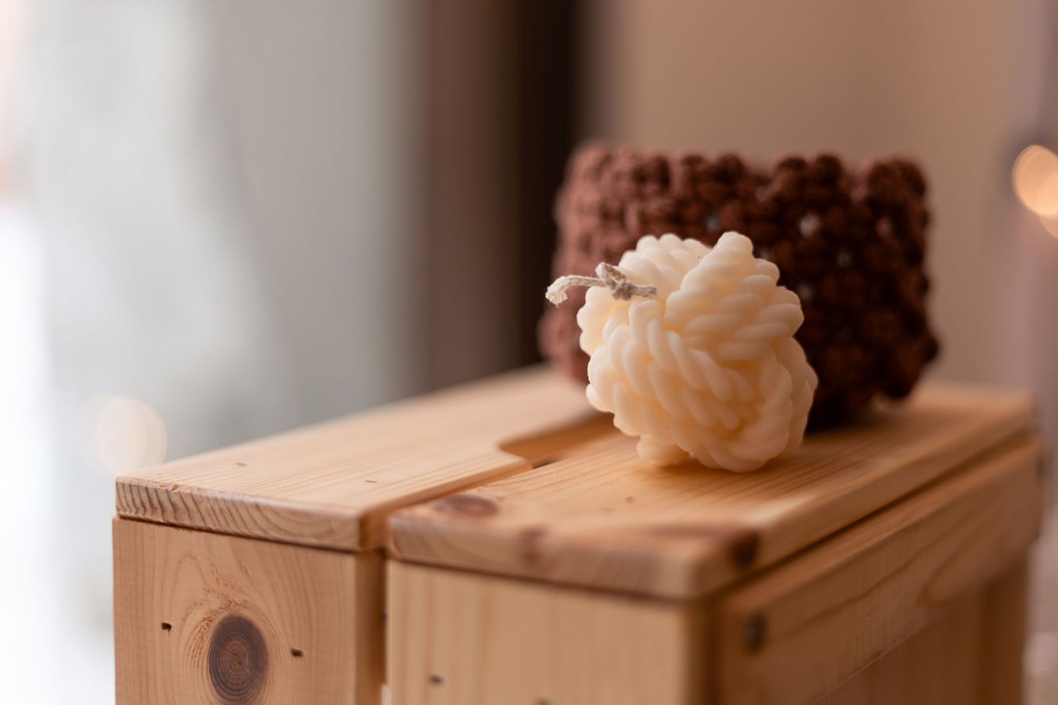 Decorative sheep-shaped white candle resting on wooden box beside textured brown candle.