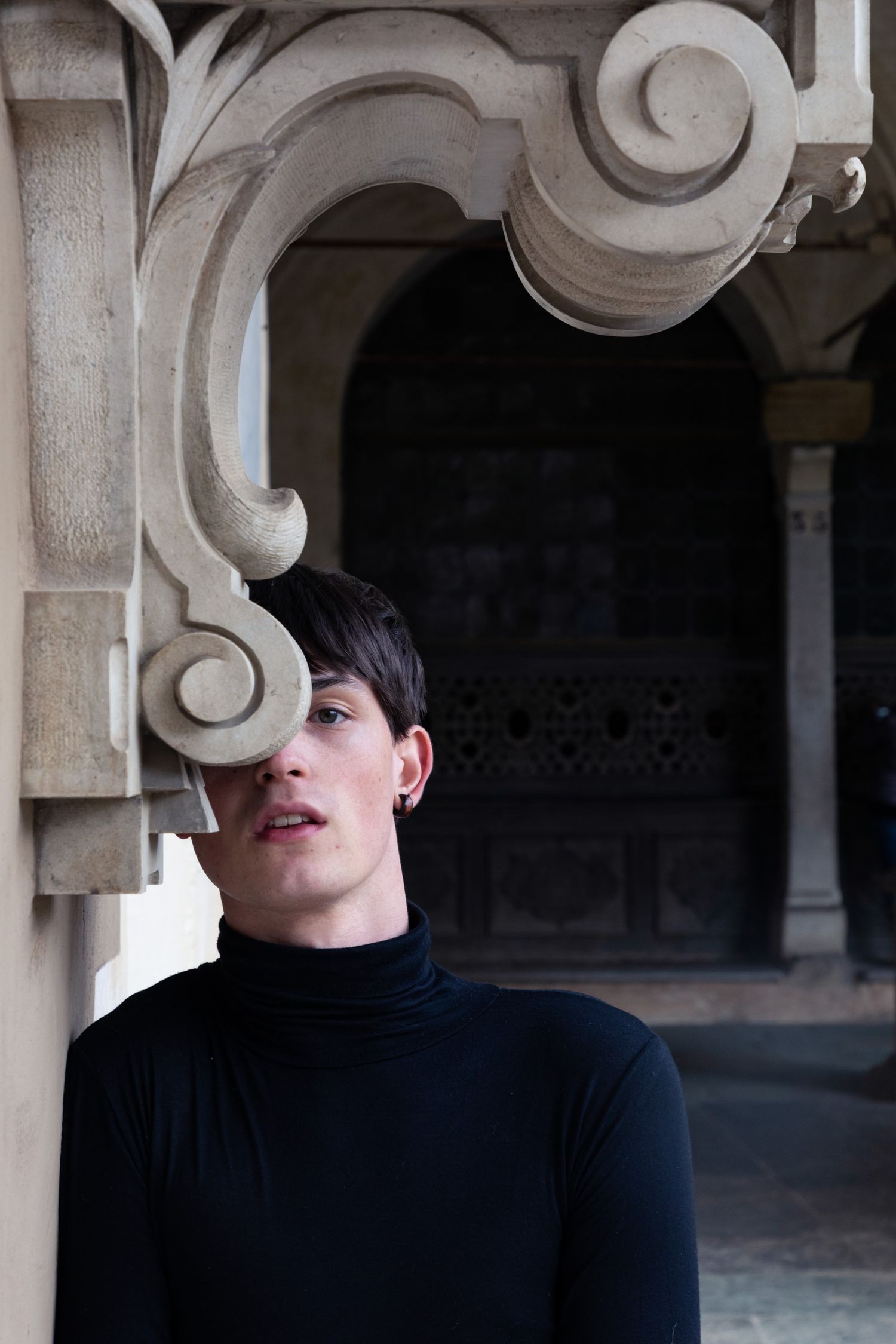 Close portrait of short-haired dancer in black turtleneck gazing upward beside ornate stone architectural detail.