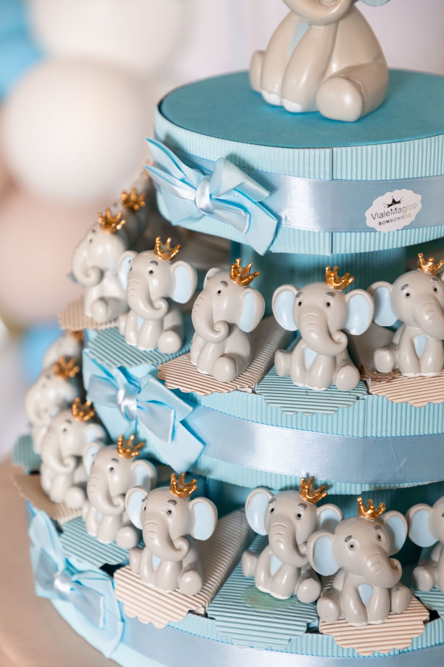 Three-tier blue and white elephant themed cake tower with crown figurines for baby shower.