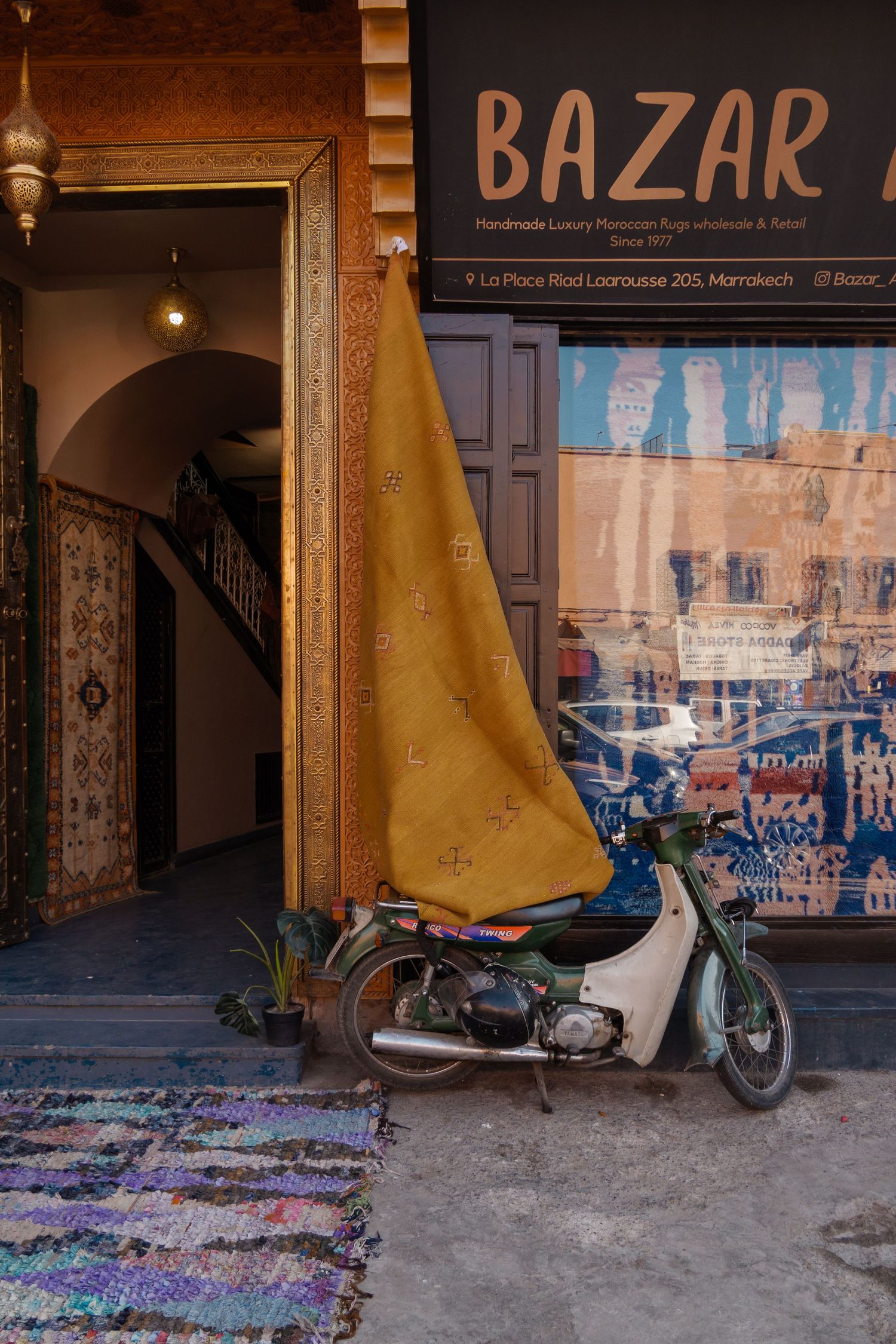 Bazar shop in Marrakech selling handmade luxury Moroccan rugs with motorcycle parked outside.