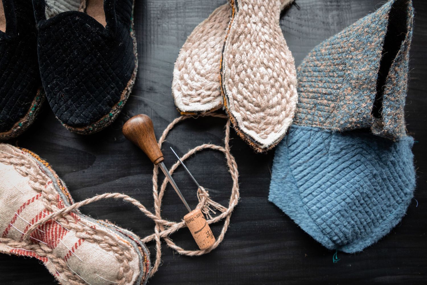 Flat lay of handmade espadrille shoes in various stages of assembly with rope, needle, and cork tool.