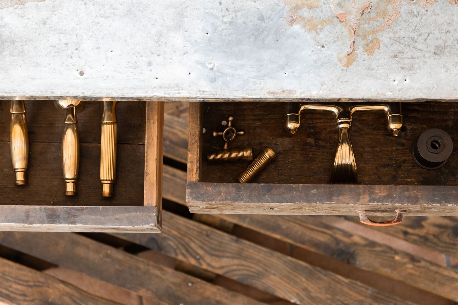 A wooden workbench drawer containing vintage brass faucet handles and plumbing tools.