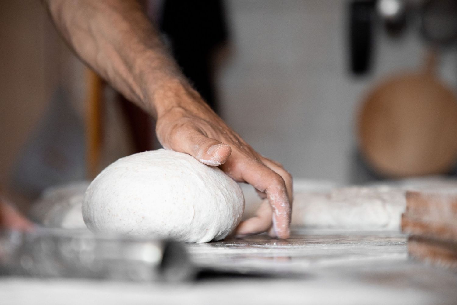 Baker's hands shaping white bread dough ball on floured surface in artisan bakery.