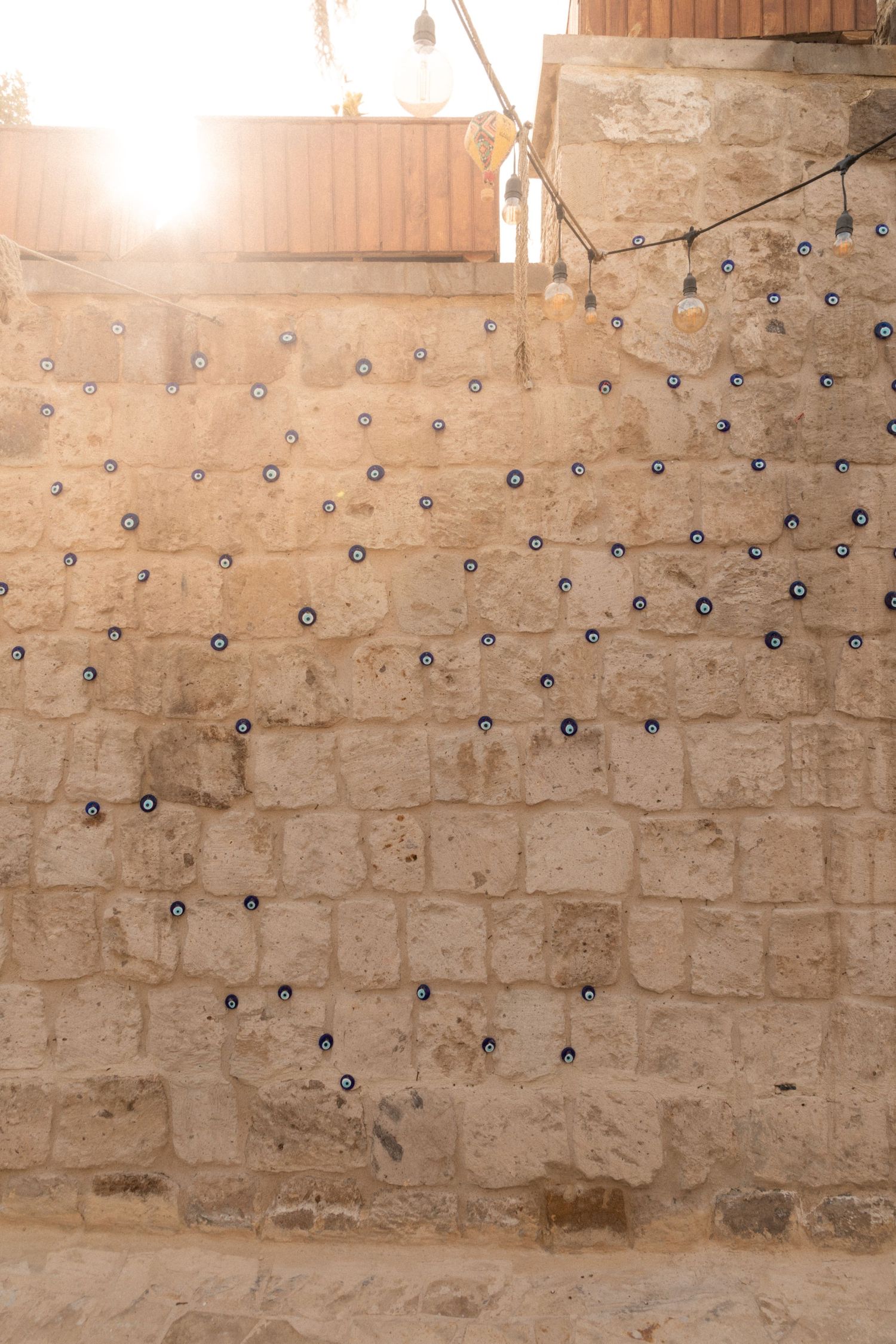 Stone brick wall covered with small blue evil eye amulets in warm sunlight in Cappadocia.