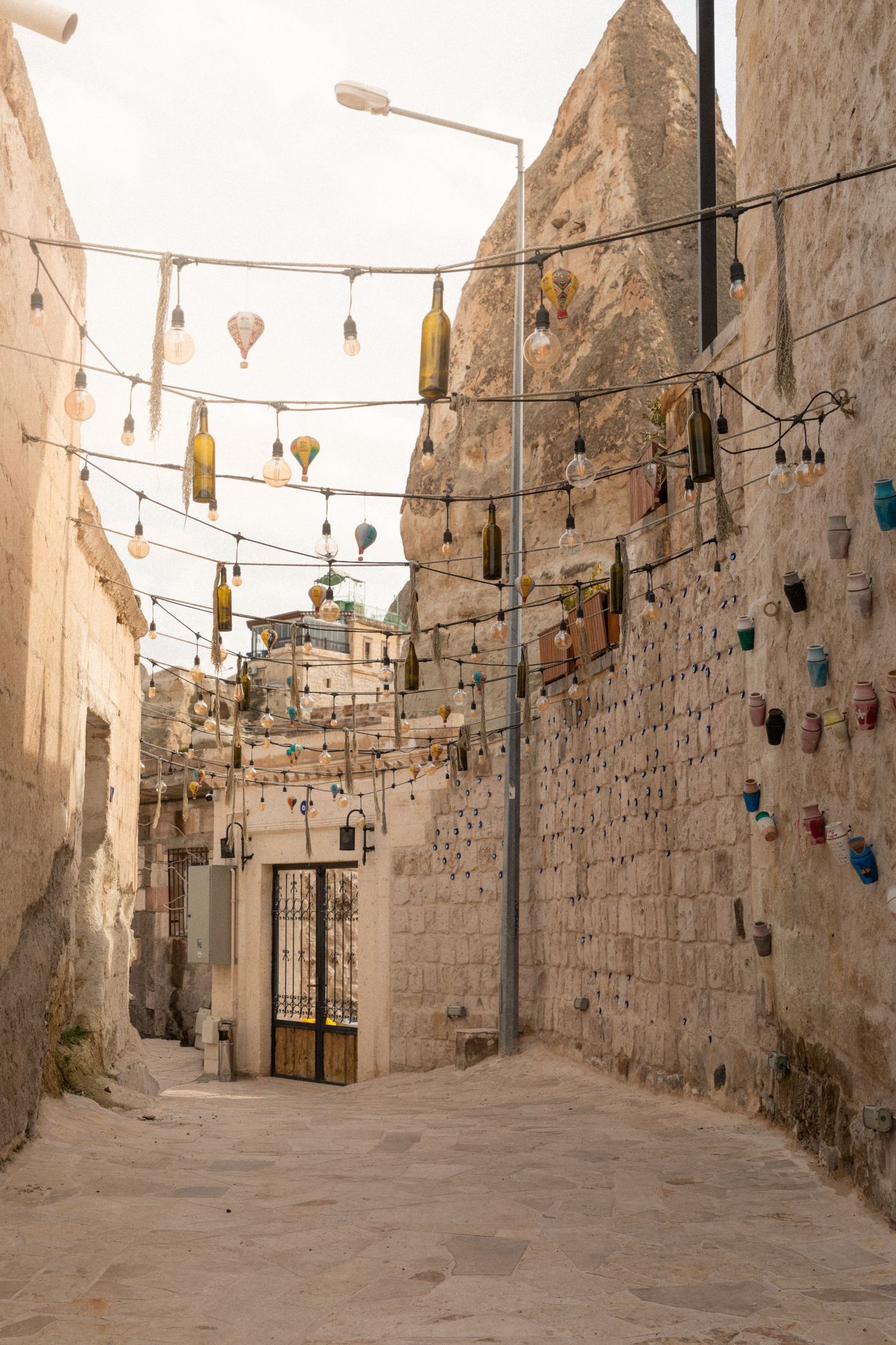 Narrow stone alley in Cappadocia decorated with hanging bottle lights and evil eye ornaments.