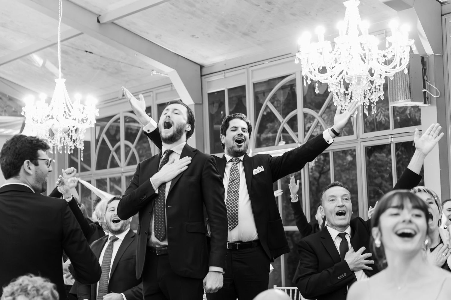 Black and white photo of joyful wedding guests singing and celebrating at reception party.