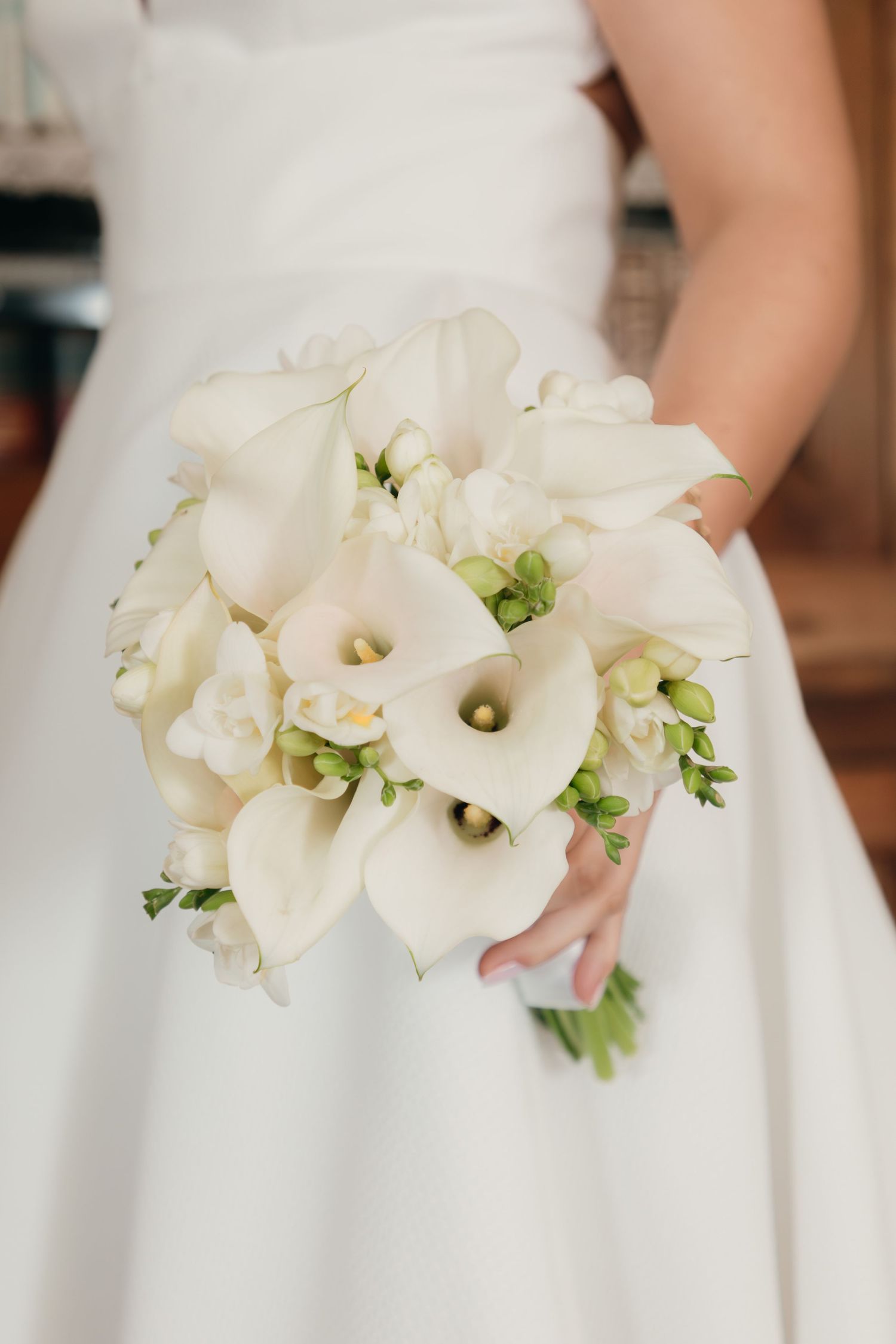 Bride holds elegant bouquet of white calla lilies and green accents against her white wedding gown.