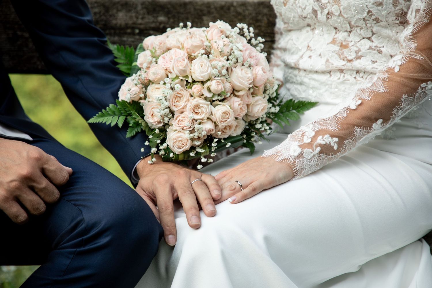 Close-up of bride and groom holding hands with elegant pink rose wedding bouquet.