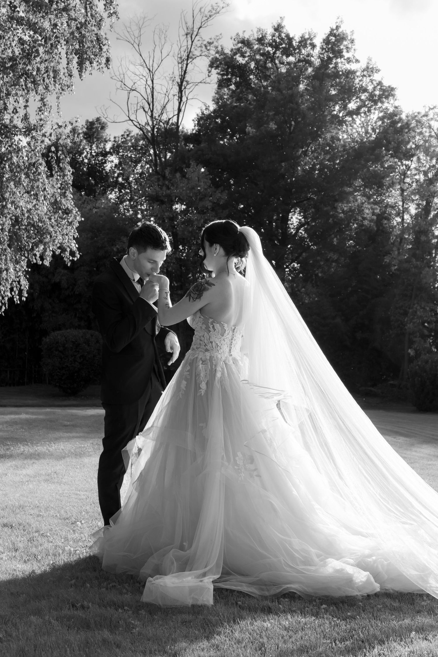 Black and white photo of groom kissing bride's hand in a lush garden setting.