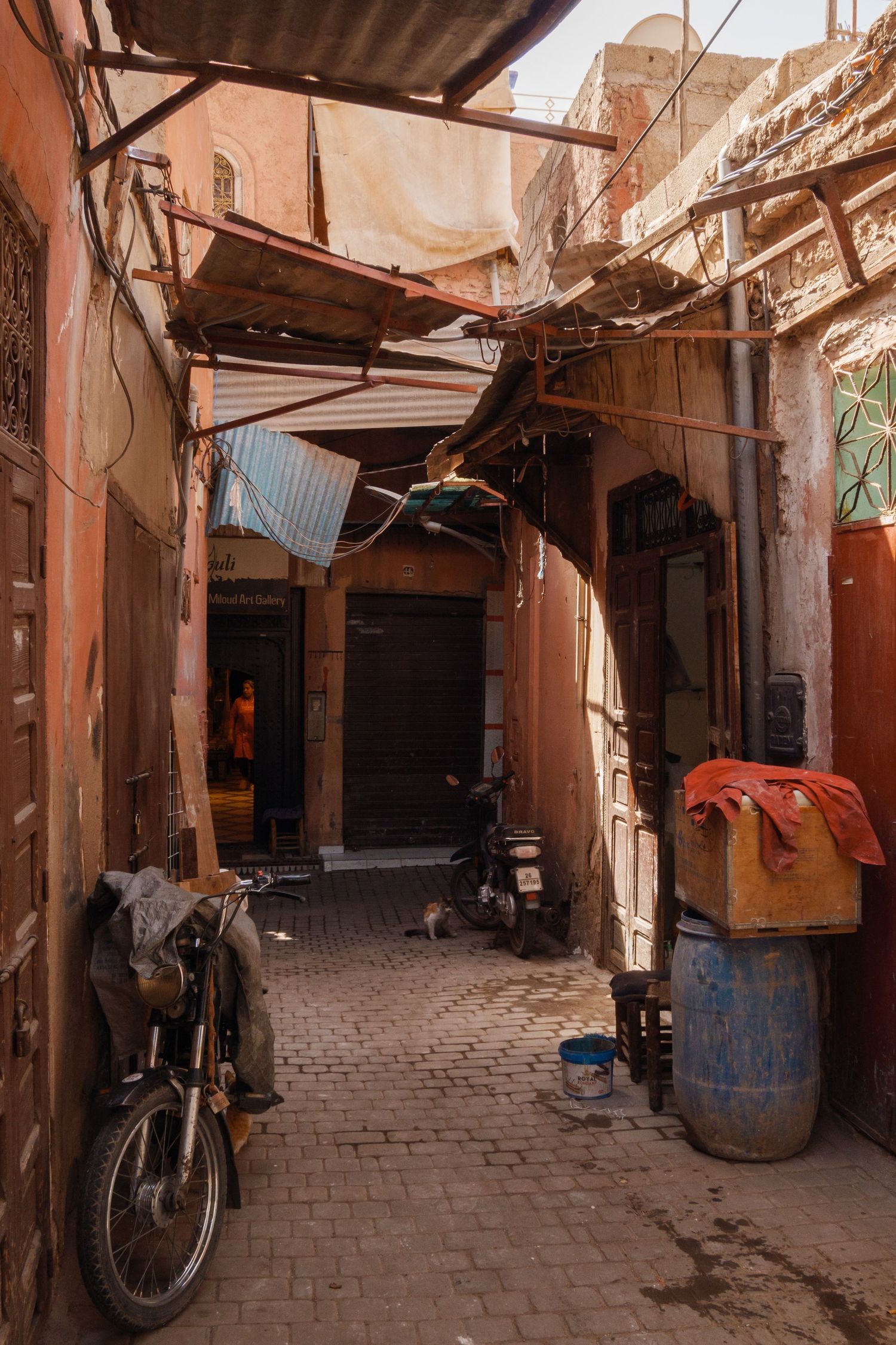 Narrow sunlit alley in a Moroccan medina with a parked motorcycle and rustic terracotta buildings.