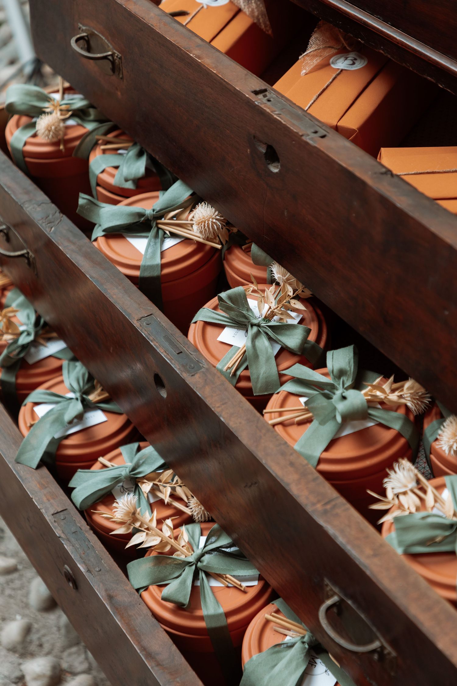 Terracotta pot wedding favors decorated with green ribbons and dried flowers displayed in wooden shelving unit.
