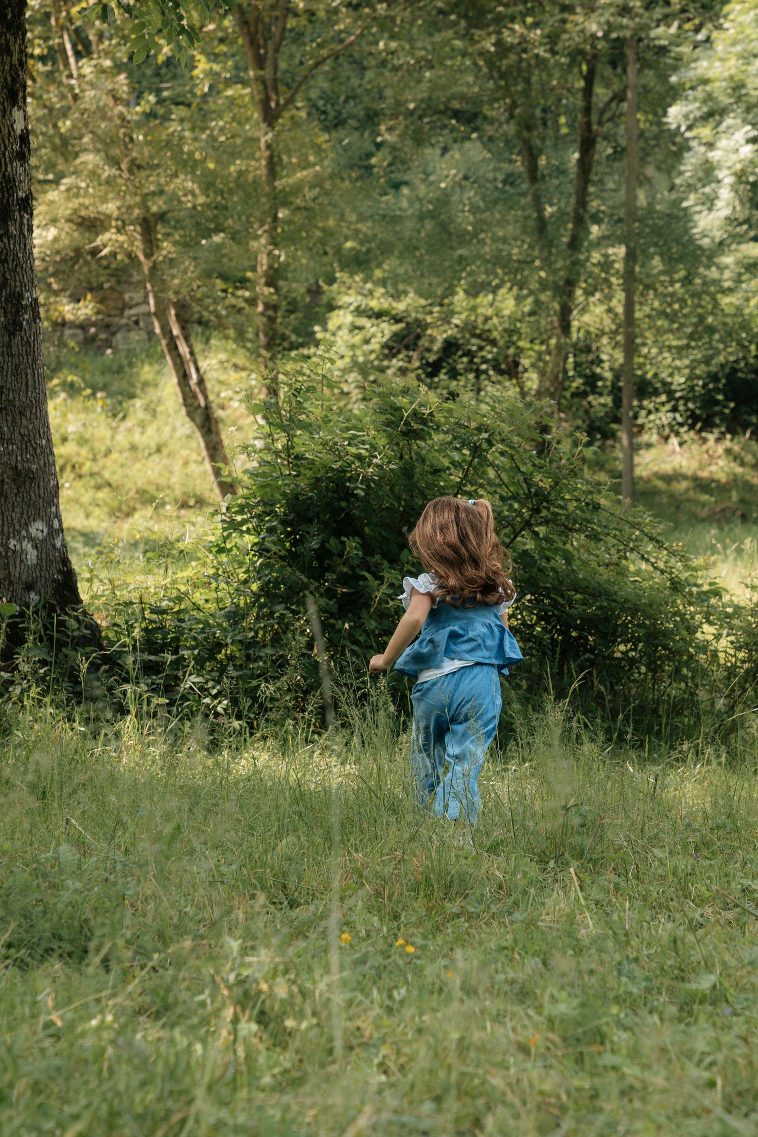 A young girl in a blue dress runs through a lush green summer forest meadow.