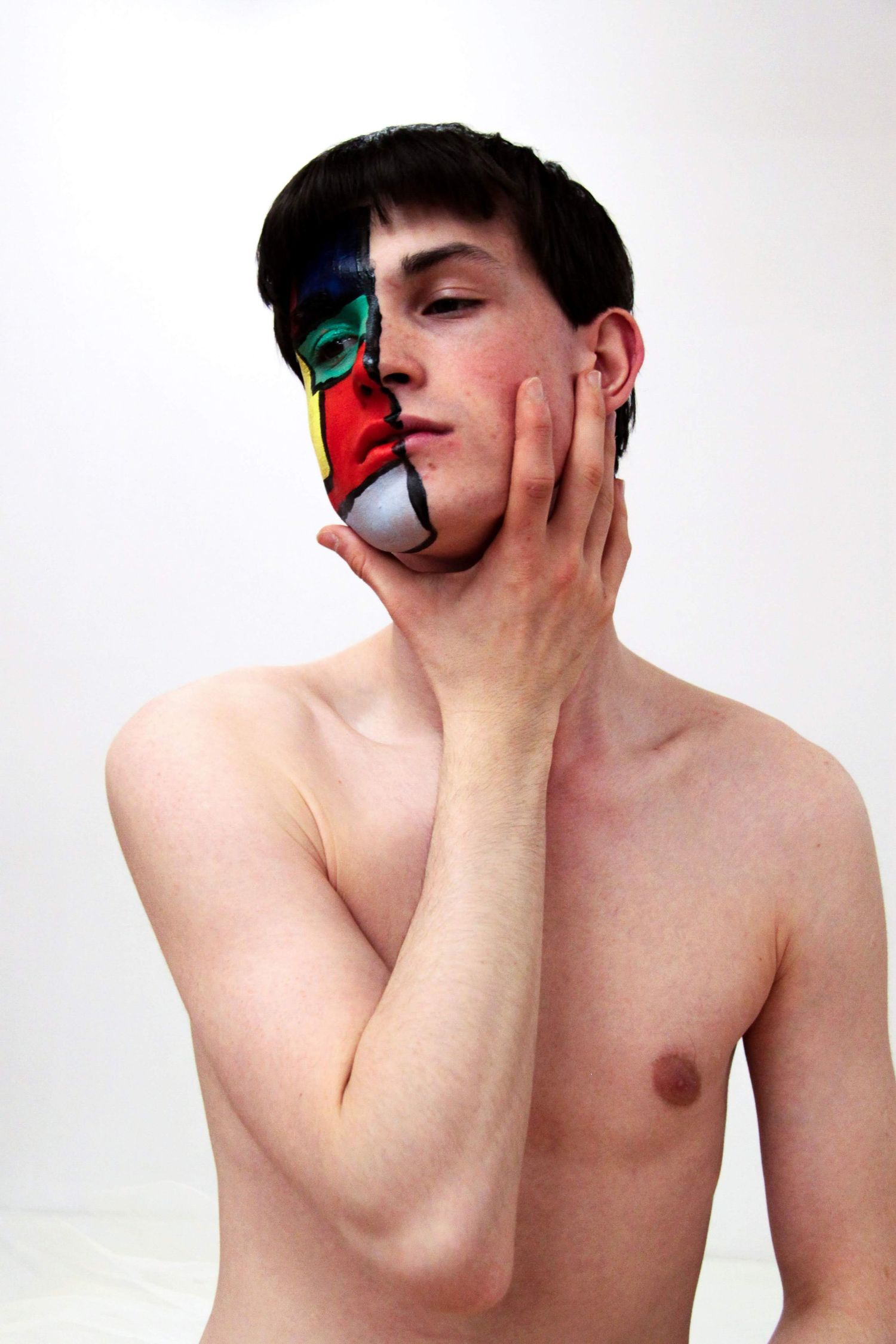 Young male performer with colorful abstract face paint on half his face against white background.