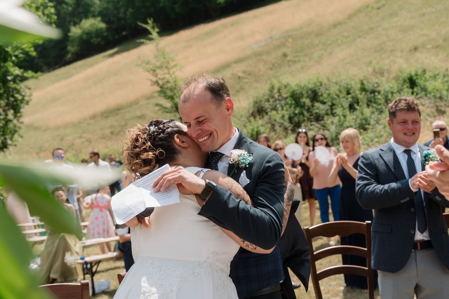 Bride and groom share emotional first hug after ceremony at outdoor wedding surrounded by applauding guests.