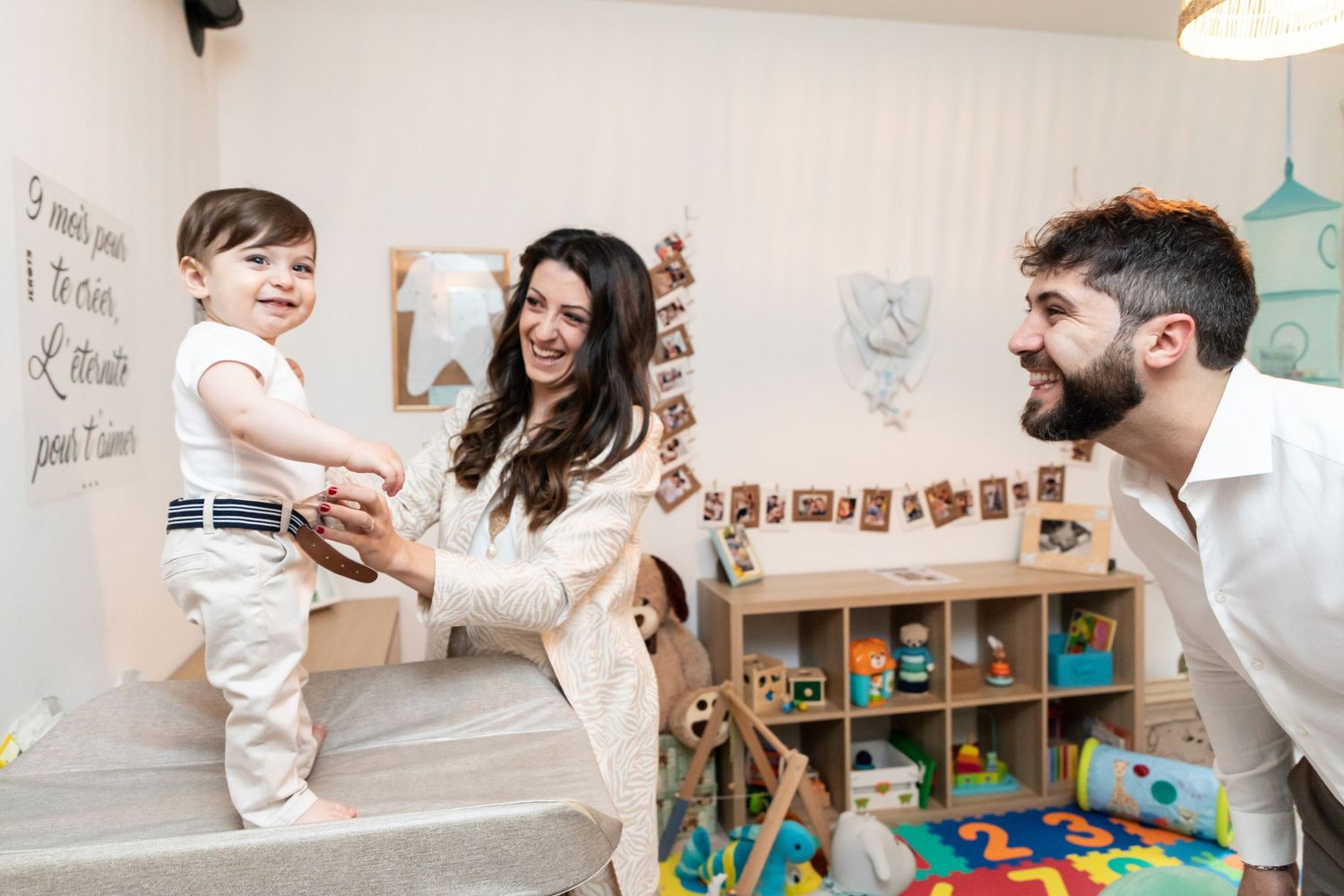 Happy family with mother, father, and toddler boy playing together in a colorful children's playroom.
