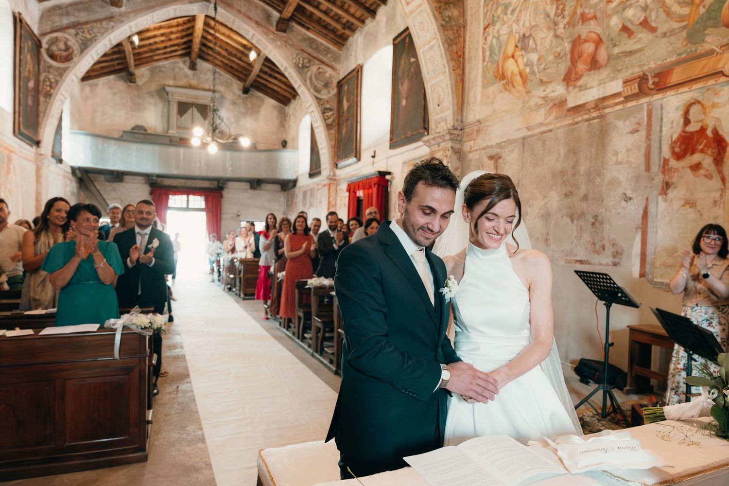 Newlyweds embrace joyfully at church altar surrounded by applauding guests after exchanging vows.