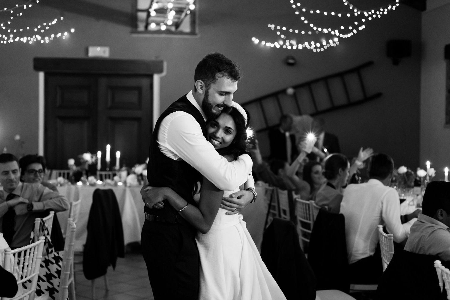 Black and white photo of bride and groom sharing first dance at wedding reception with fairy lights.