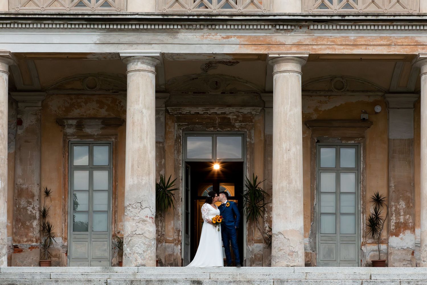 Elegant wedding couple pose between grand stone columns of a historic classical building at dusk.