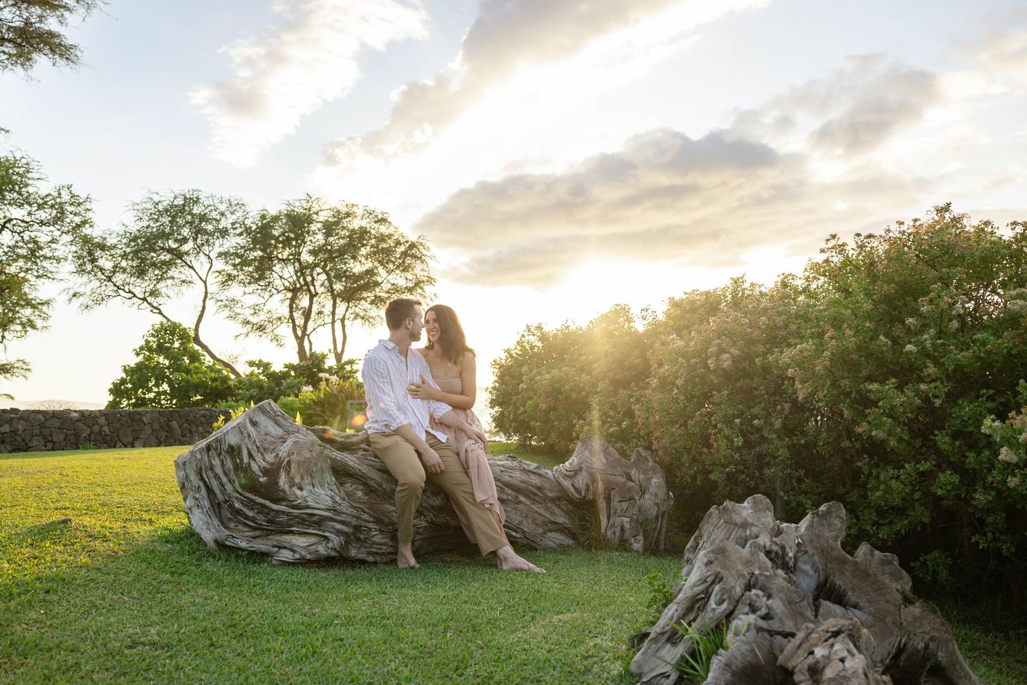 Romantic couple sitting together on driftwood log at sunset in lush Hawaii garden.