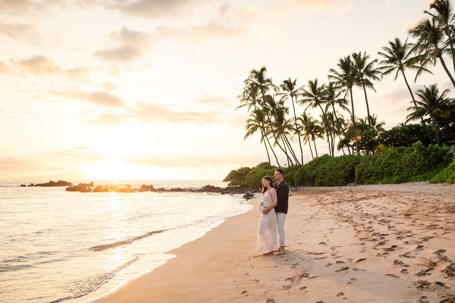 Couple embracing on a serene Hawaiian beach surrounded by palm trees at sunset.