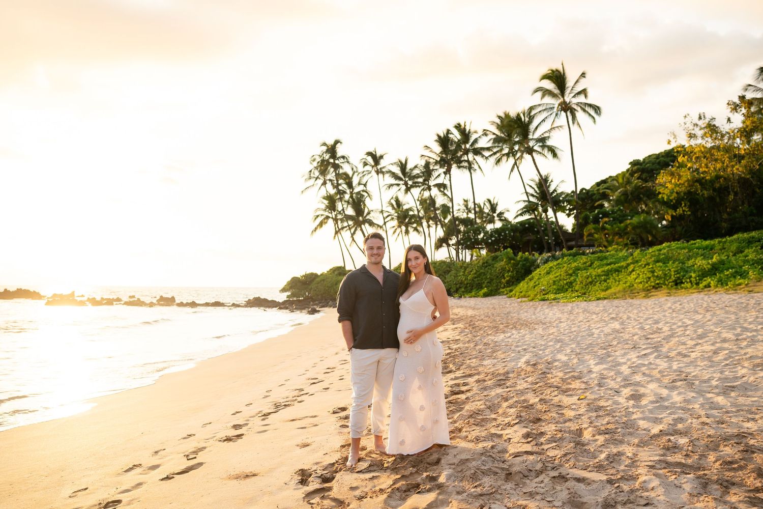 Couple posing together on a sandy Hawaiian beach during a stunning golden sunset with palm trees.