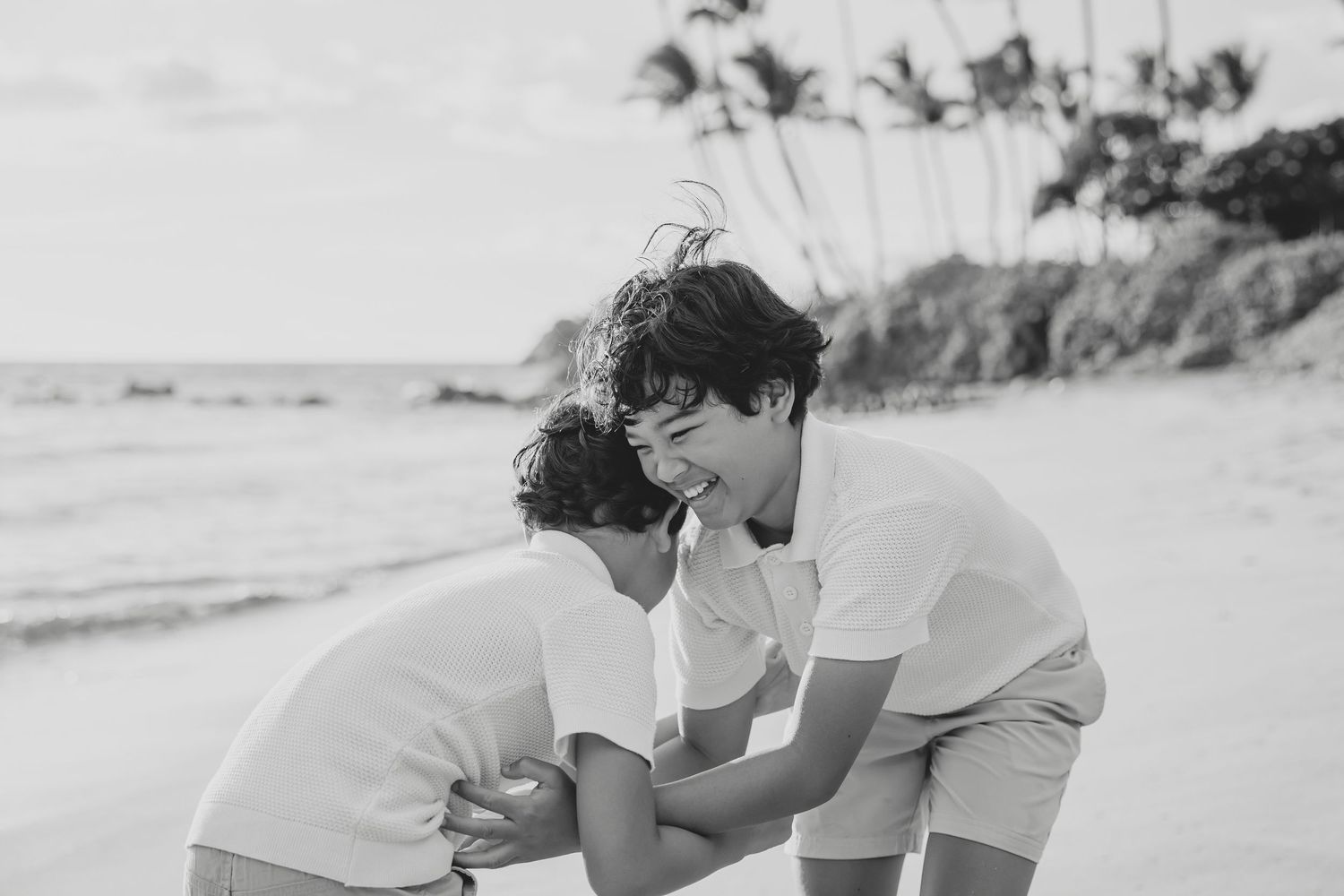 Two children laugh and play together on a tropical beach in black and white.