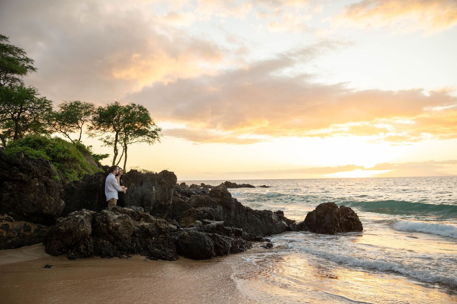 Person sitting alone on rocky Hawaii beach at sunset with dramatic colorful sky.