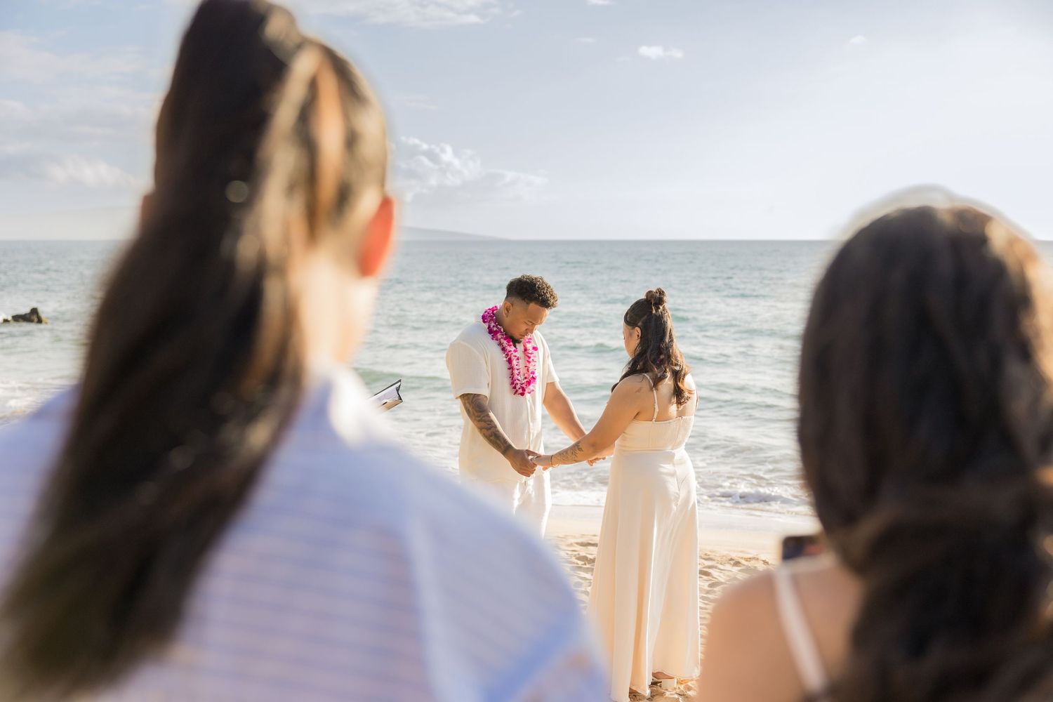 Couple exchanging vows at a beach wedding ceremony in Maui, Hawaii, with guests watching in the foreground.