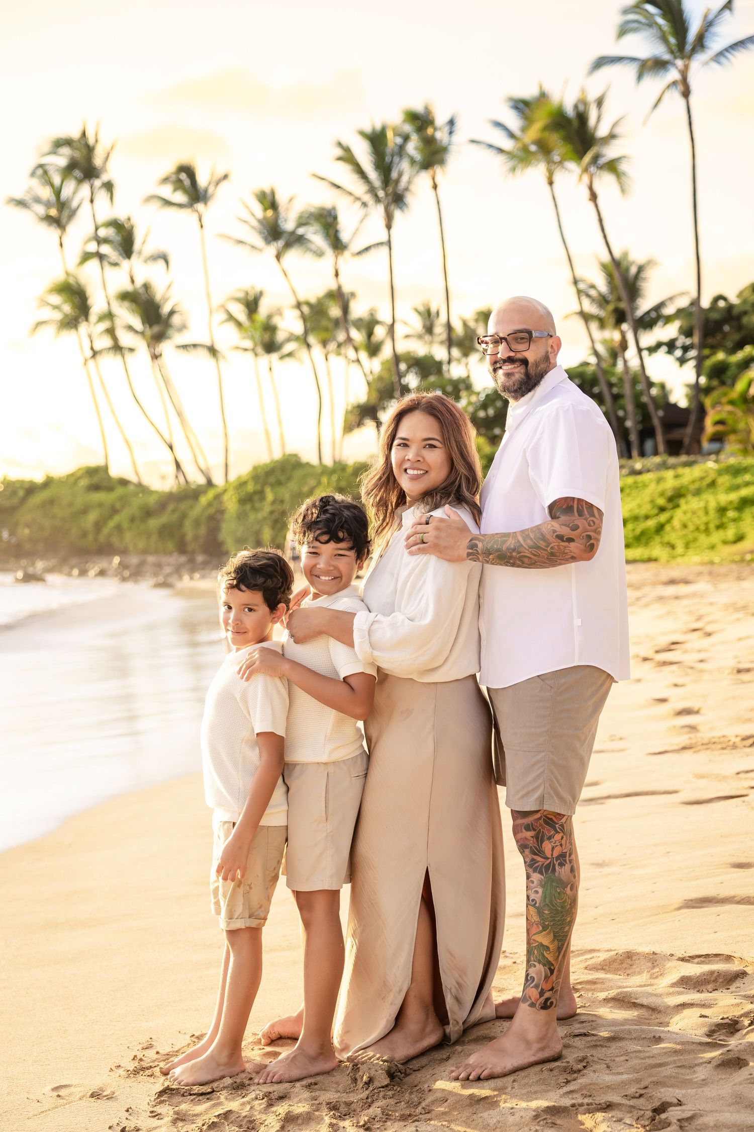 Family of four posing together on a Hawaii beach with tall palm trees at sunset.