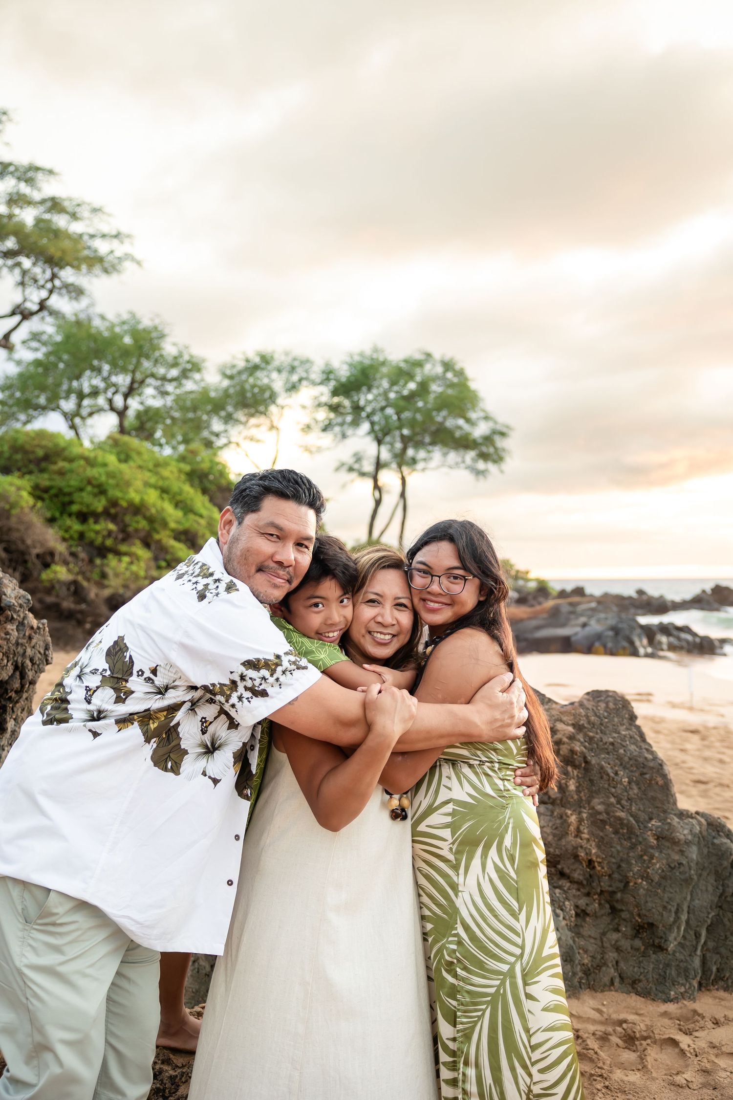 Joyful Hawaiian family of four sharing a warm group hug on a beach at sunset.