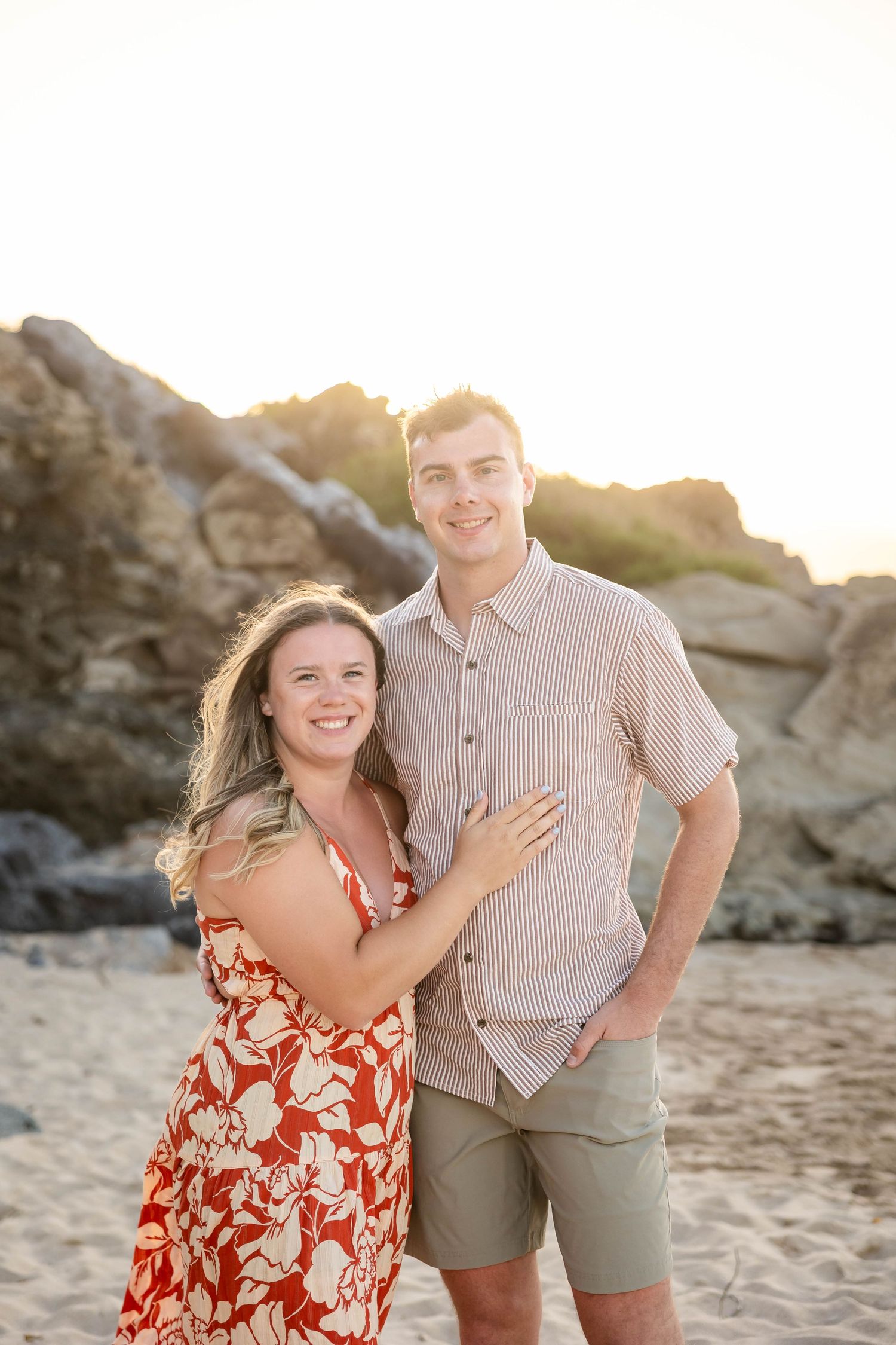 Smiling couple posing together on sandy beach at golden sunset.