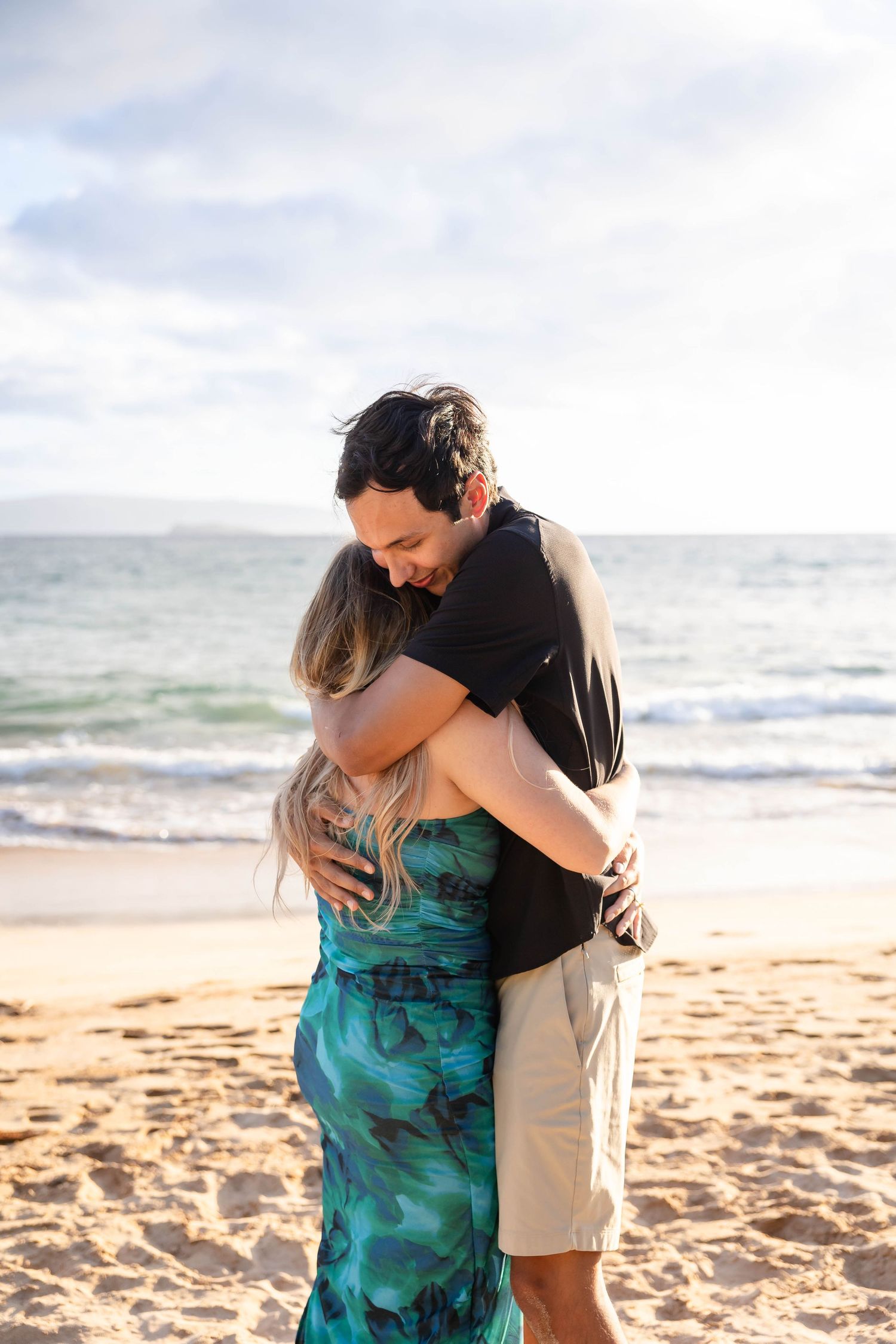 Happy couple embracing on a sunny Hawaiian beach with ocean waves and blue sky in the background.