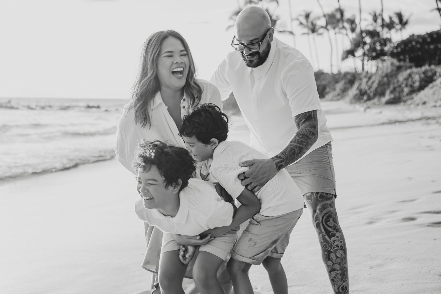 Joyful family of four plays together on a sunny beach in black and white photo.