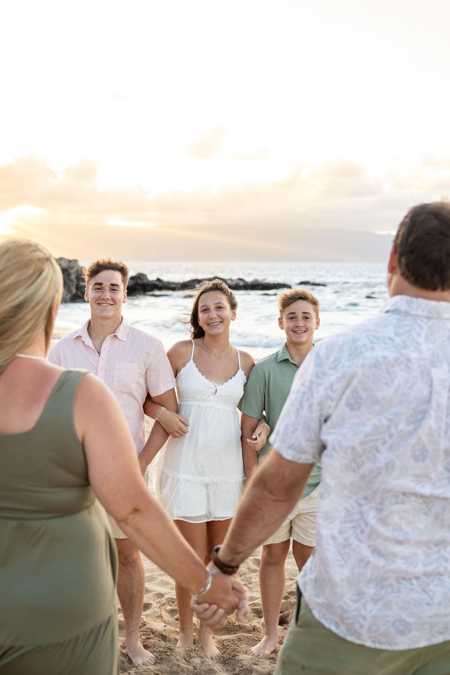 Family of five holding hands on a Hawaii beach at golden sunset hour.