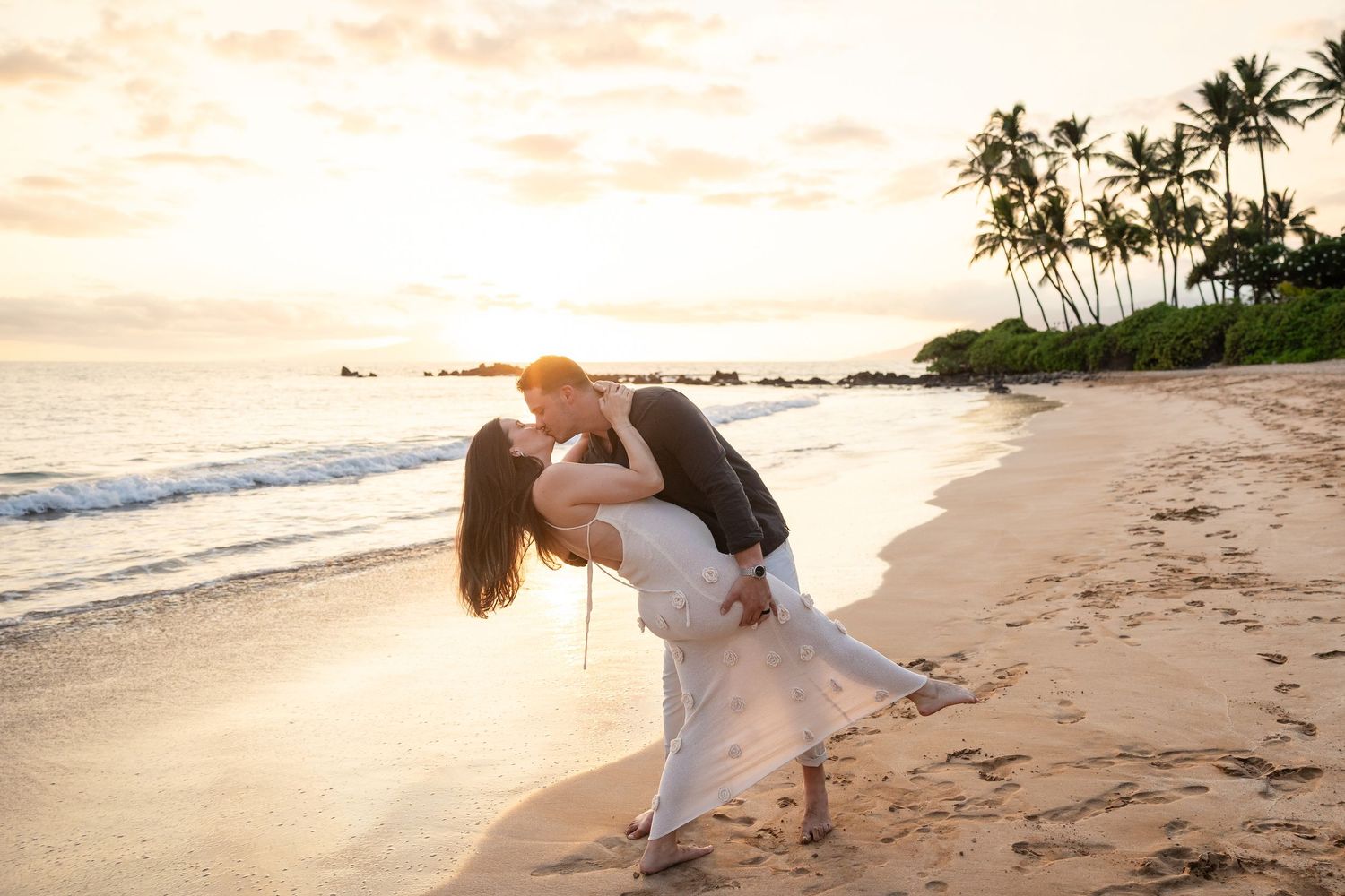 Couple sharing a romantic dip kiss on a tropical beach at sunset.