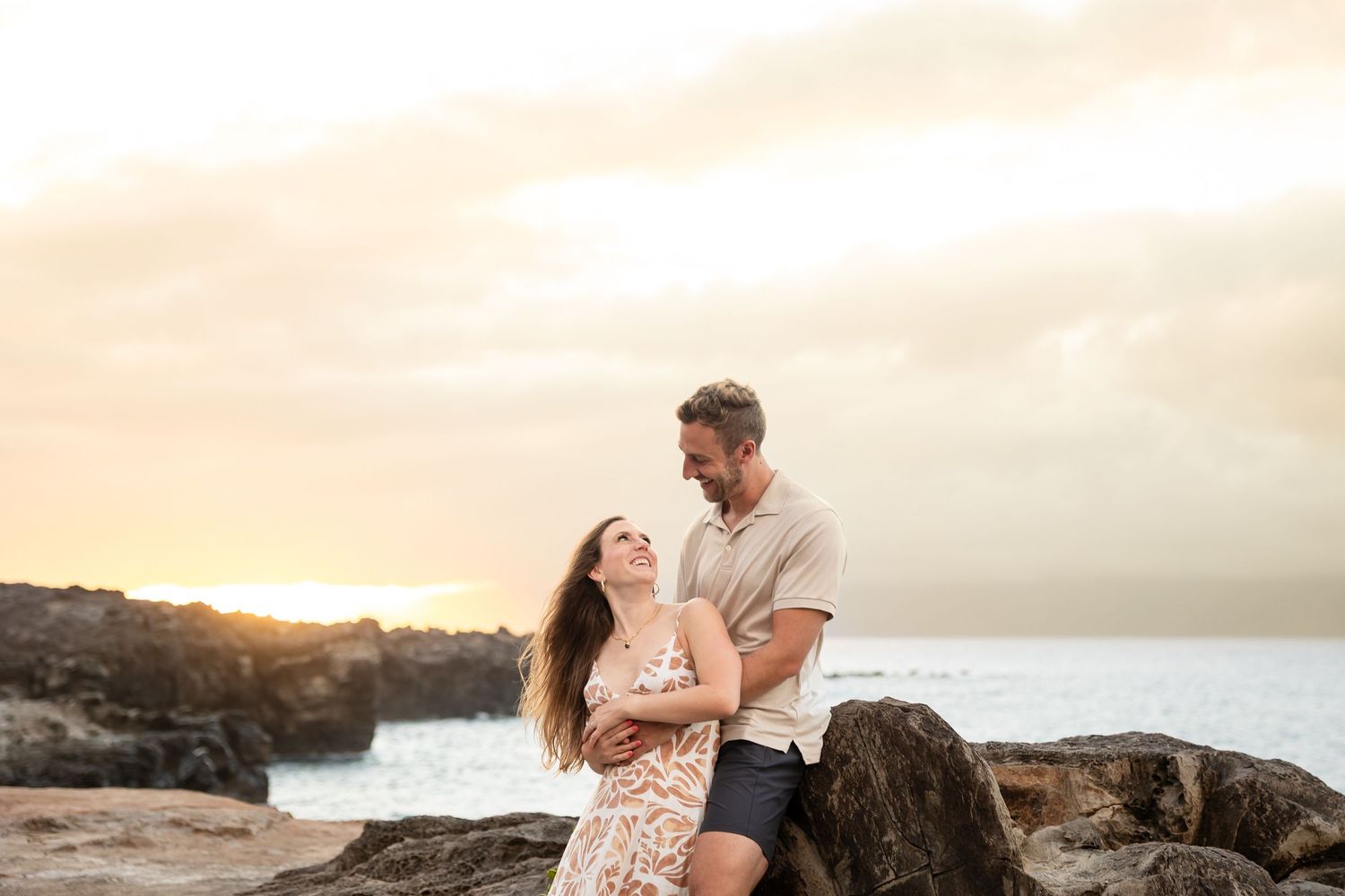 Couple laughing and embracing on lava rocks at a beautiful Hawaiian beach sunset.