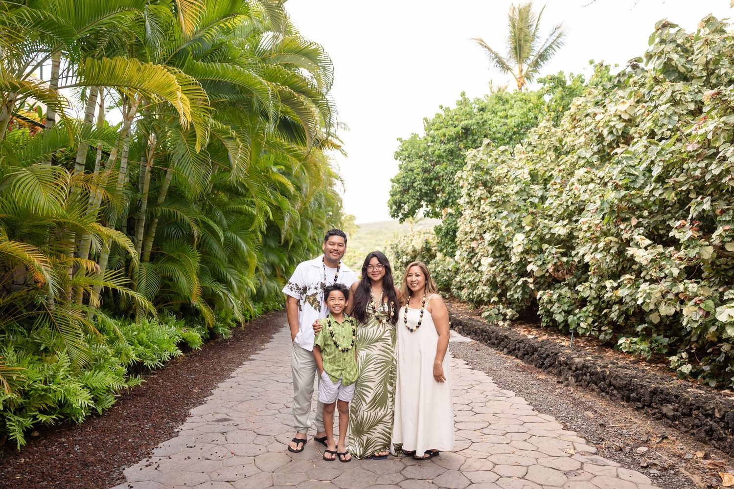 Happy family of four posing on a tropical Hawaiian garden path lined with palms.