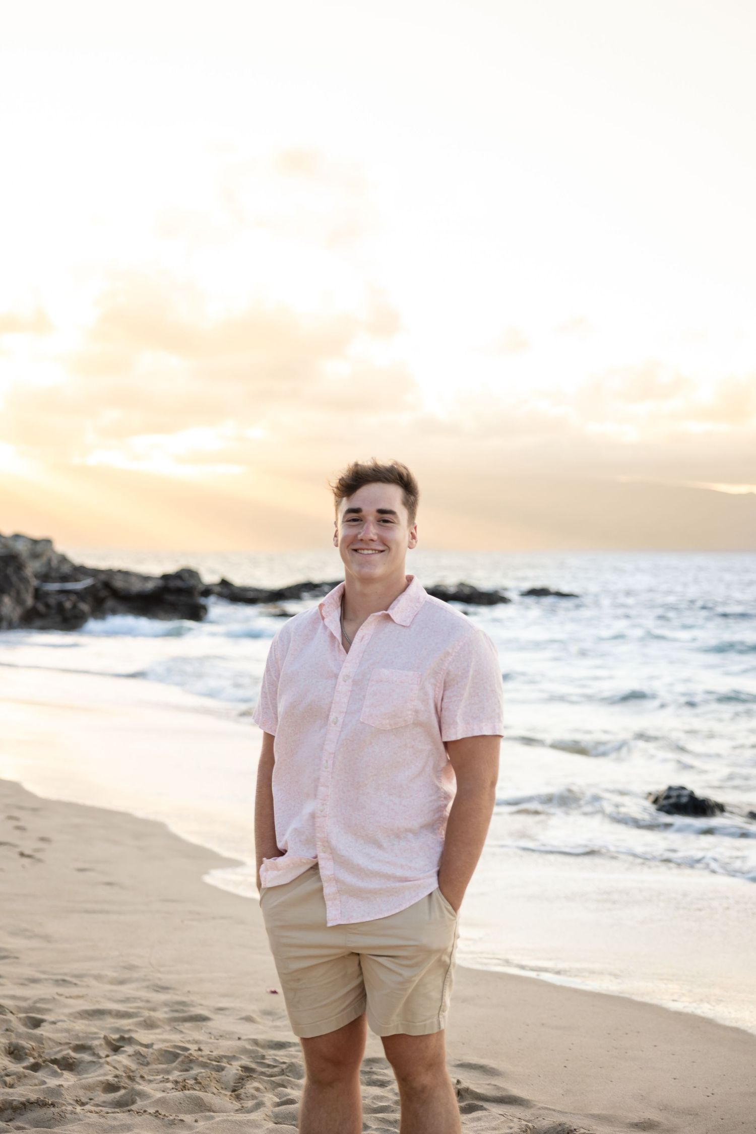 Smiling young man in pink shirt posing on a Hawaiian beach at sunset.