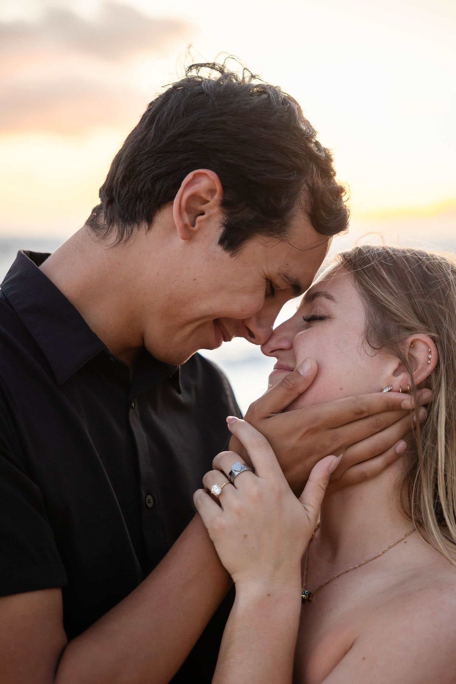 Romantic couple sharing an intimate moment at sunset on the beach, woman wearing engagement ring.