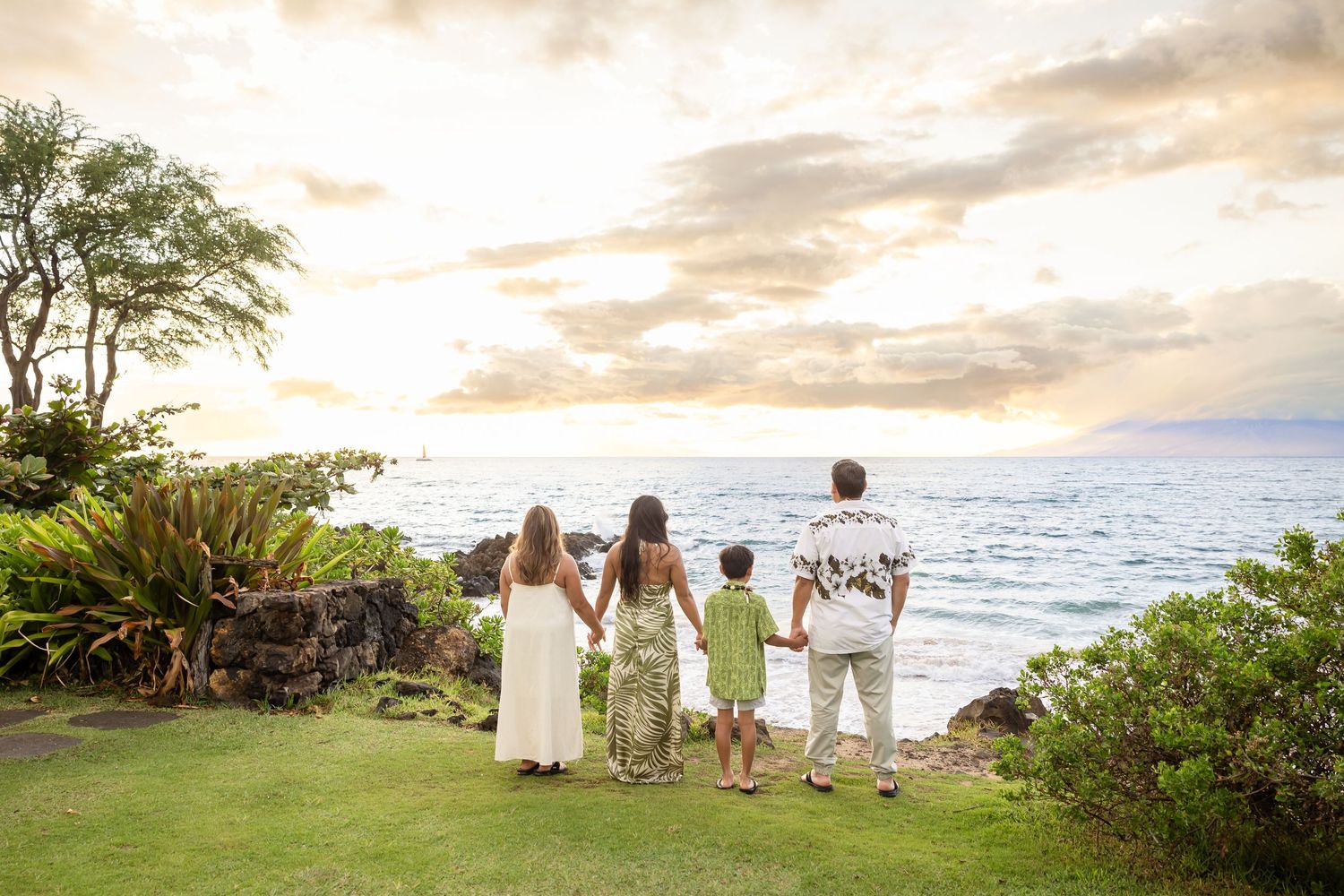 Family of four holding hands while gazing at the ocean during a Hawaii sunset.