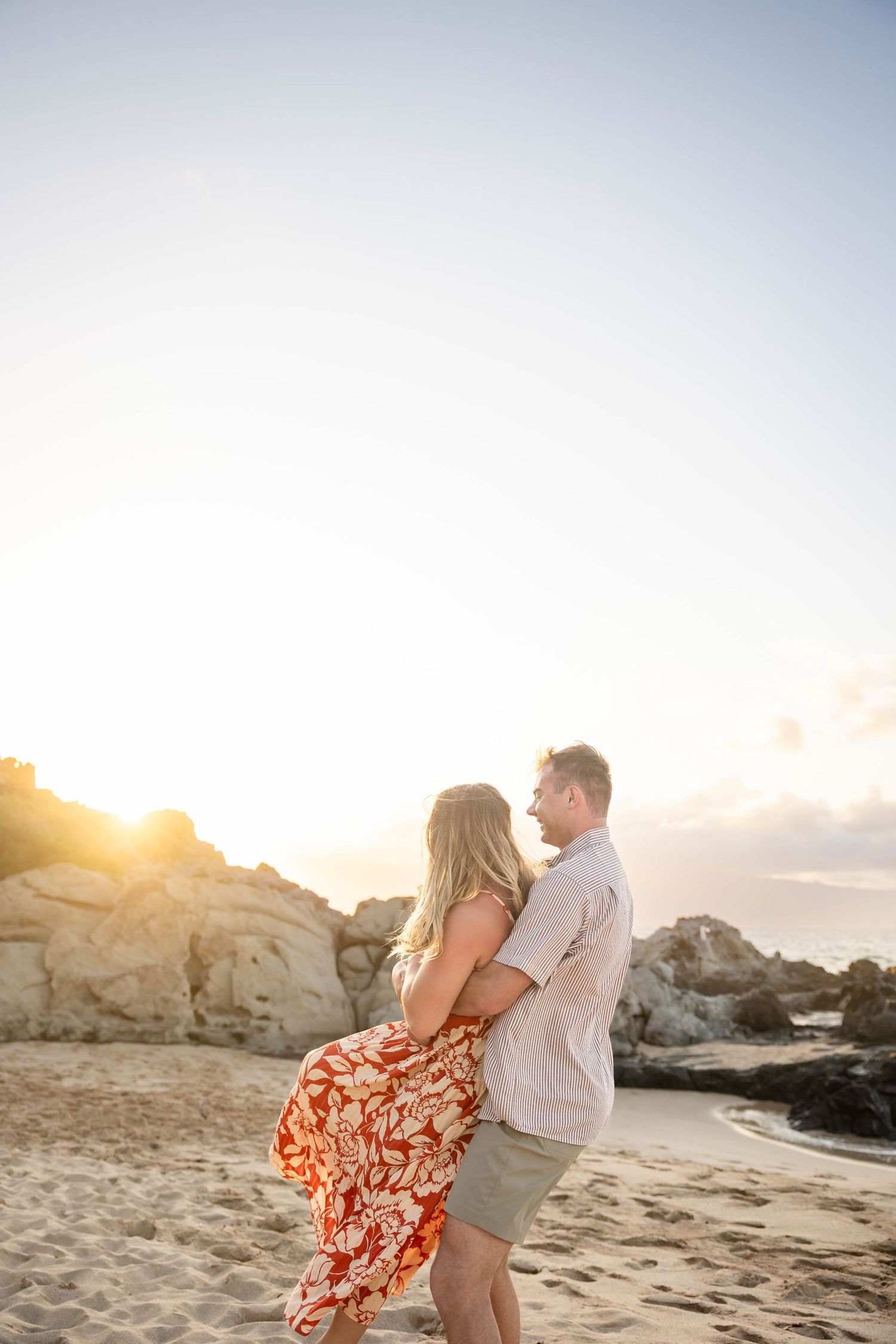 Couple embracing on a sandy Hawaiian beach during a warm sunset.